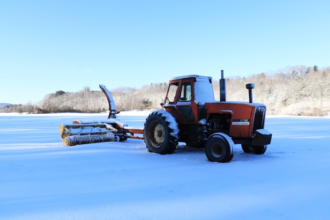 En röd traktor med ett bakmonterat redskap på ett snöigt fält, vilket illustrerar den mångsidiga användningen av traktorer året runt.