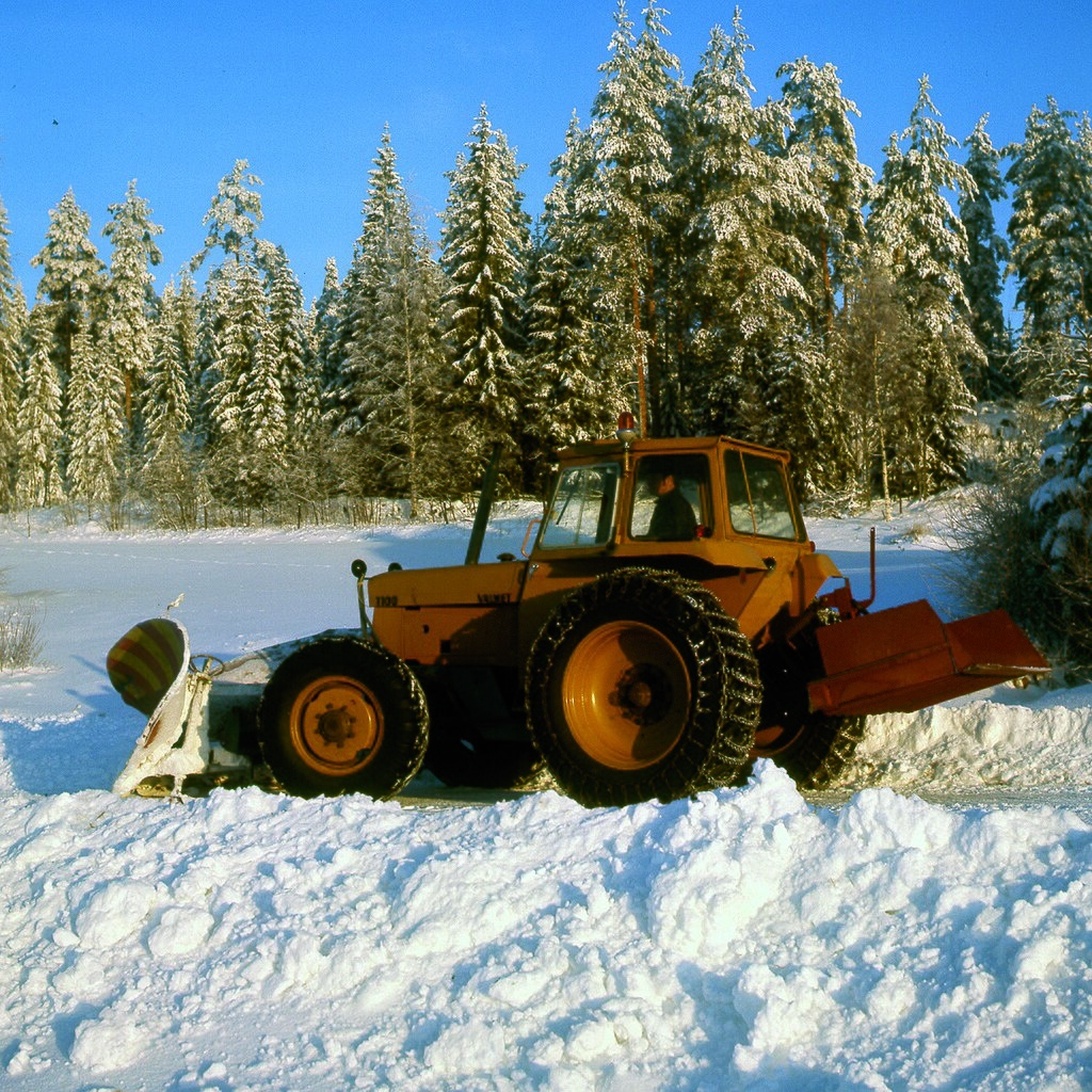 En orange traktor med ett frontmonterat snöblad som effektivt arbetar sig igenom djup snö i ett vinterlandskap.